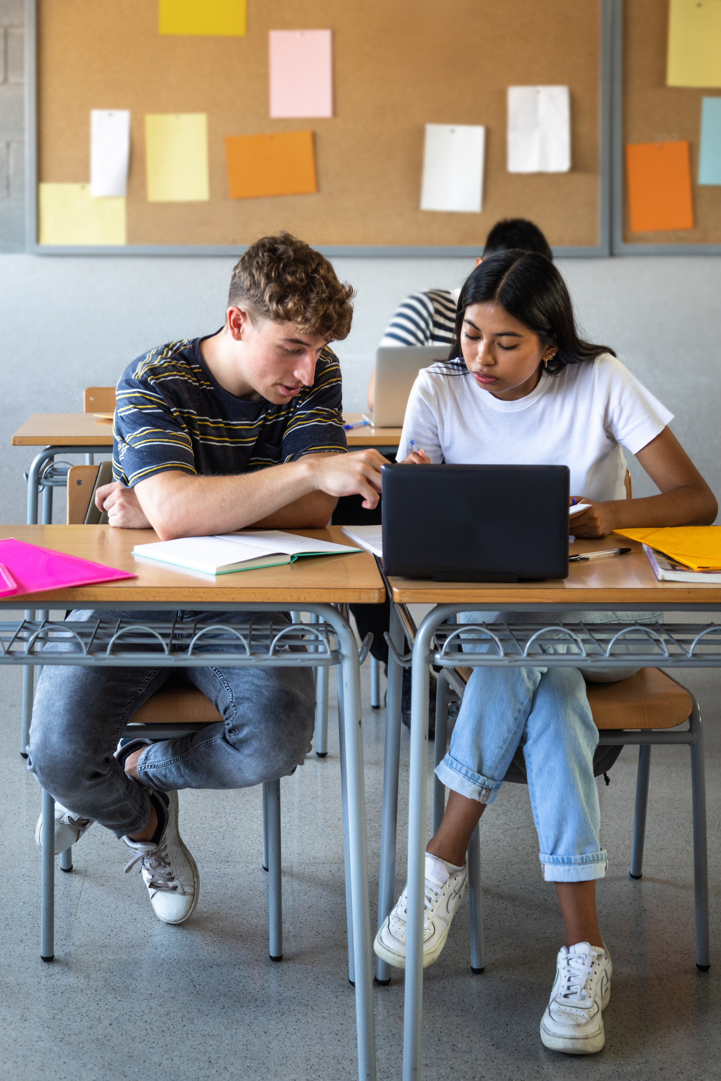 Teen boy and native american female high school students in class working together using laptop. Vertical.